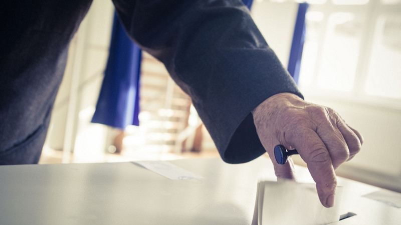 Eine Person wirft einen Wahlzettel in eine Wahlurne.