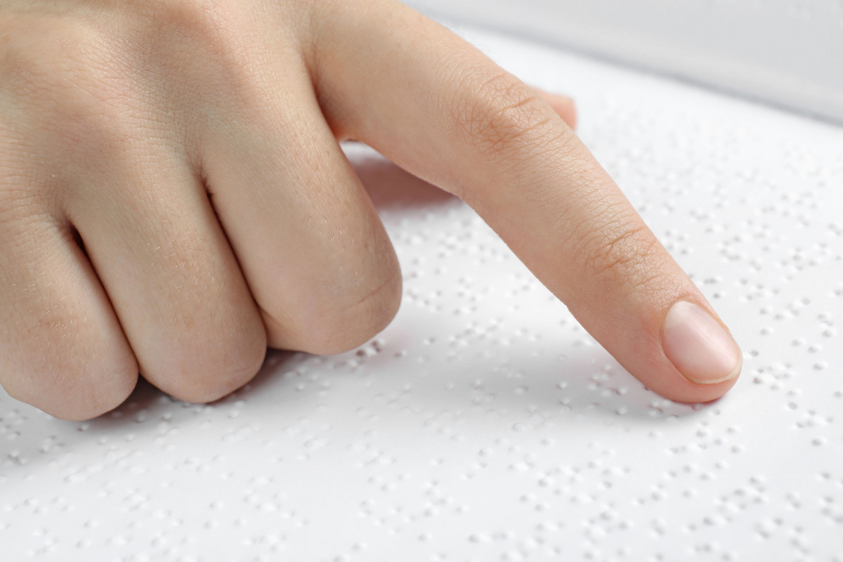 Das Bild zeigt einen Finger, die einen Text in Braille-Schrift liest