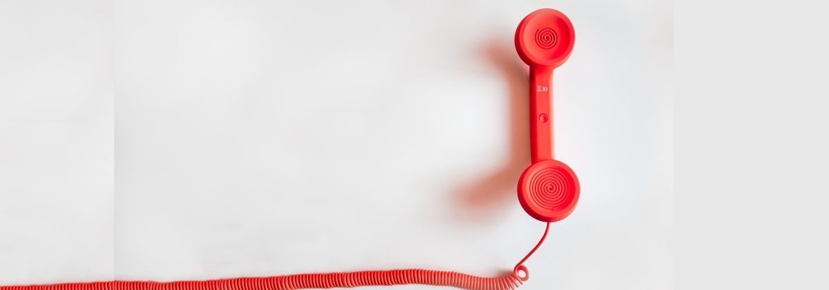 Das Bild zeigt einen roten Telefonhörer mit Schnur.