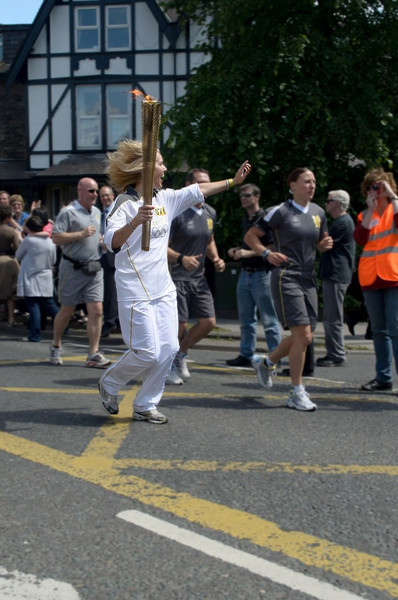 Das Foto zeigt eine Frau, die das olympische Feuer bei einem Fackellauf trägt. Die Frau läuft.