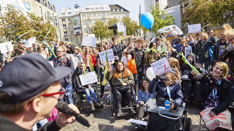 Das Foto zeigt Menschen bei der Kundgebung zum Protesttag am 5. Mai 2019 auf dem Münsterplatz Bonn. Foto: Aktion Mensch