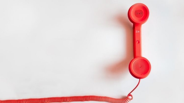 Das Bild zeigt einen roten Telefonhörer mit Schnur.