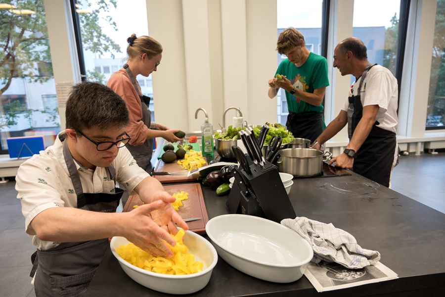 Vier Menschen bereiten Paprika, Avocado und Salat vor.