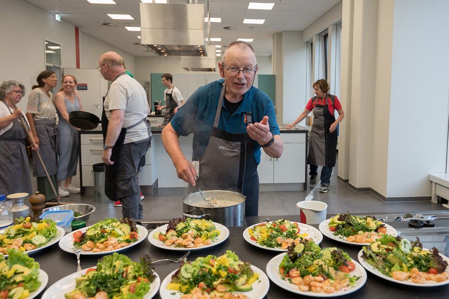 Diedrich Hespen schmeckt die Soße ab. Im Vordergrund ist die angerichtete Vorspreise zu sehen: Teller mit Shrimps und Salat stehen bereit.