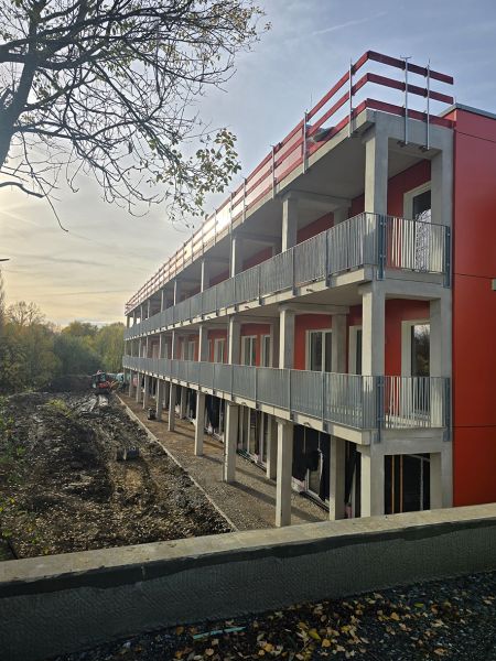 Dieses Bild zeigt die Gebäudefassade mit rotem Anstrich, sowie frisch montierte Geländer an den Laubengängen.