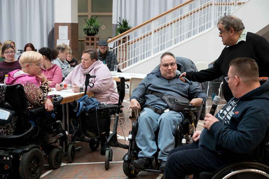 Moderator Jürgen hält das Mikro für einen Rollstuhlfahrer aus dem Publikum.