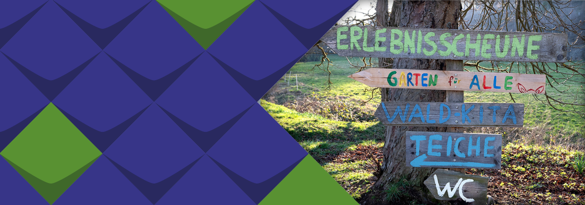 Holzschilder an einem Baum weisen den Weg zum Garten für Alle und zu anderen Orten im Naturschutzzentrum