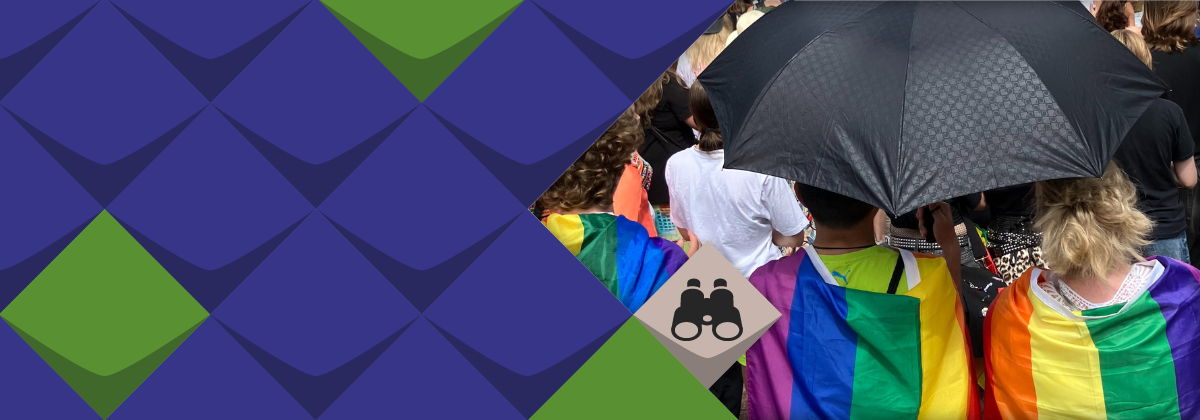 Zwei Menschen mit umgehängten Regenbogenfahnen sind von hinten zu sehen. Sie halten einen Sonnenschirm über sich