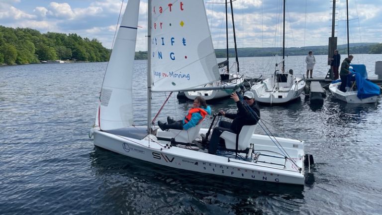 Zwei Personen in einem Segelboot, auf dem auch mit Menschen mit körperlichen Einschränkungen den Sport betreeiben können.