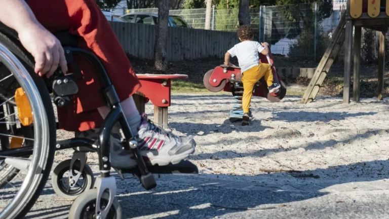 Im Vordergrung die Räder eines Rollstuhls, im Hintertergrund ein spielender Junge