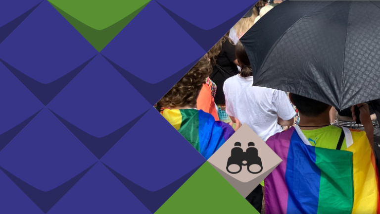 Zwei Menschen mit umgehängten Regenbogenfahnen sind von hinten zu sehen. Sie halten einen Sonnenschirm über sich